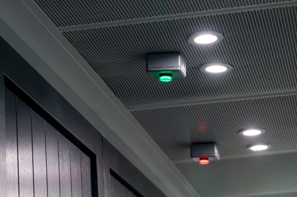 Ceiling-mounted occupancy sensors with illuminated red and green indicators alongside recessed lighting