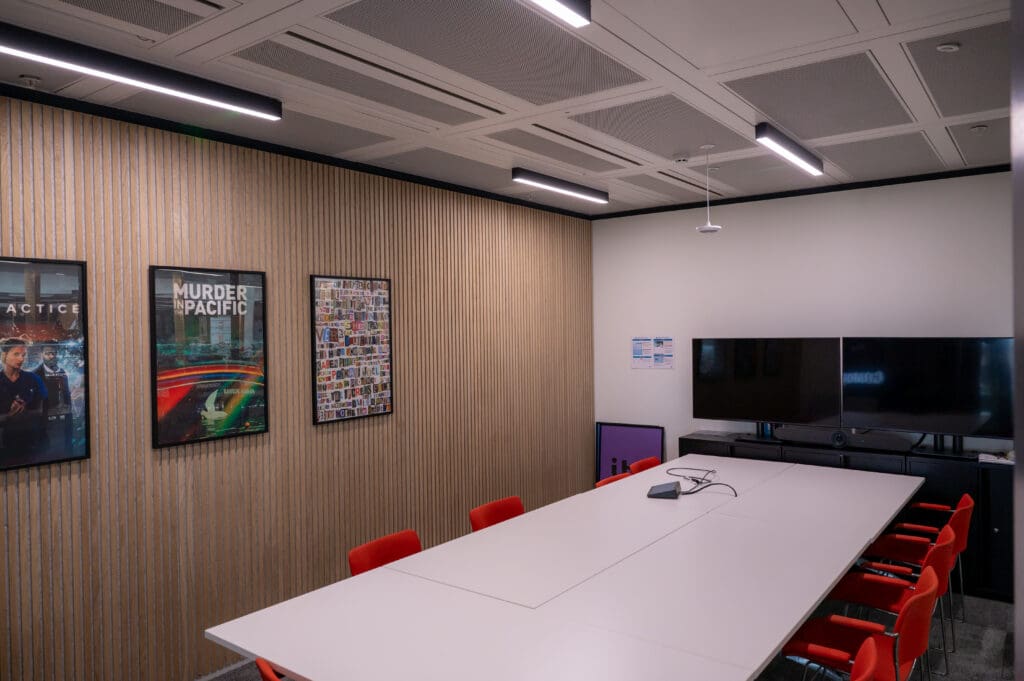 Contemporary meeting room with dual wall-mounted screens, acoustic slatted wood panelling, and integrated LED lighting