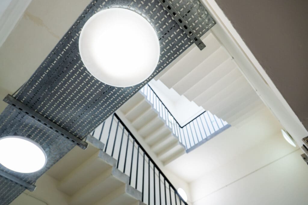 Metal cable tray with integrated circular LED bulkhead lights installed along a stairwell ceiling